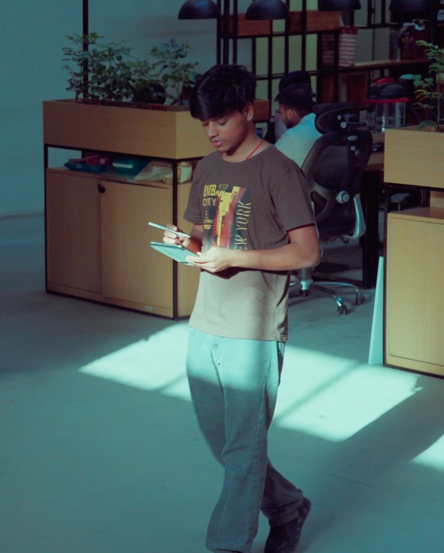 Pavan walking across the office through patches of sunlight, writing on a tablet